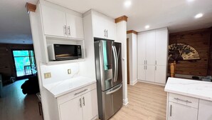 A modern kitchen with white cabinetry, stainless steel appliances, and a wooden accent wall. - Luxury Log Cabin with work spaces, generator and car charger  (Tiny Township)