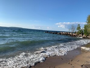 A beach with clear water, a rocky shoreline, and sparse vegetation. - Luxury Log Cabin with work spaces, generator and car charger  (Tiny Township)