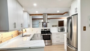 A modern kitchen with white cabinets, stainless steel appliances, and a marble countertop. - Luxury Log Cabin with work spaces, generator and car charger  (Tiny Township)