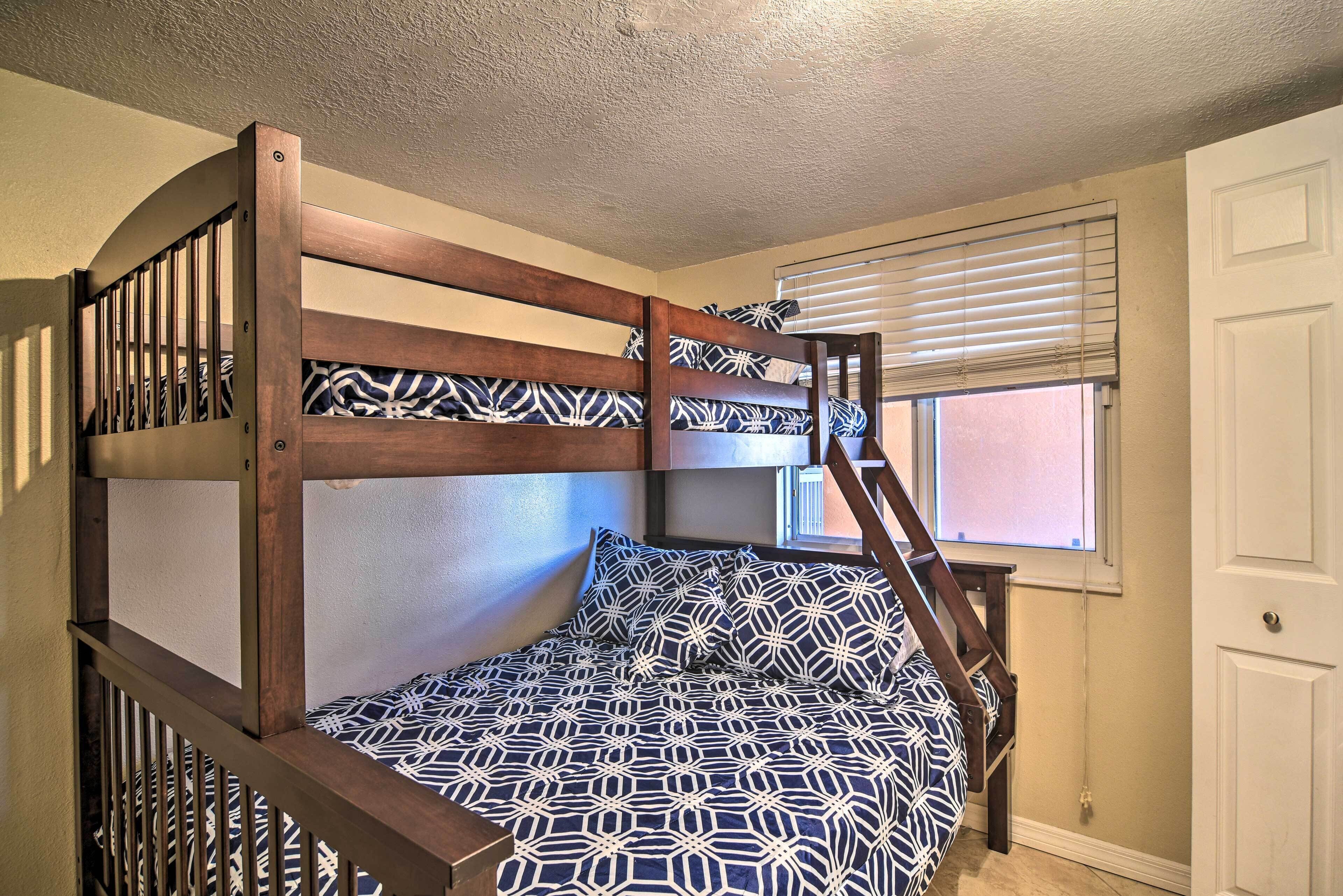 Una cama litera con ropa de cama estampada, una ventana con persianas y una puerta blanca.