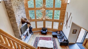 A spacious loft-style living area with a stone fireplace, a large chandelier, and a view of the forest through large windows. - 2nd Largest Home @ Camelback “Occupancy is 20 with day guests included” (Tannersville)