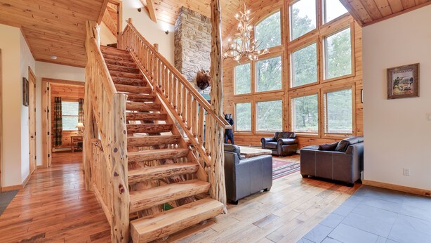 A spacious living area with a wooden staircase, large windows, and a stone fireplace. - 2nd Largest Home @ Camelback “Occupancy is 20 with day guests included” (Tannersville)