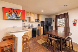 A compact kitchen with a microwave, refrigerator, and a dining area with a table and stools.