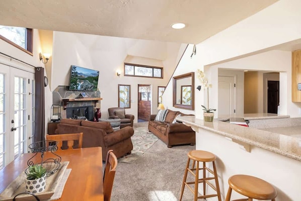 A spacious living area with a fireplace, sofas, a dining table, and a kitchen area with a countertop and stools.