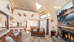 A spacious living room with a fireplace, a large TV, and ski equipment on the wall. - Snow Summit Dome Home. Walk to Snow Summit. HotTub (Big Bear Lake)
