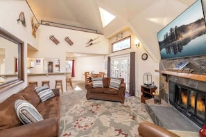 A spacious living room with a fireplace, a large TV, and ski equipment on the wall.