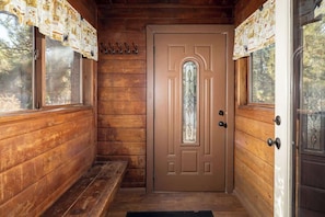 A wooden cabin interior with a door, windows, and a bench.