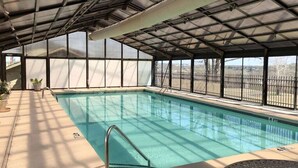 Una piscina interior con techo cubierto, paredes de vidrio transparente y vistas al exterior.
