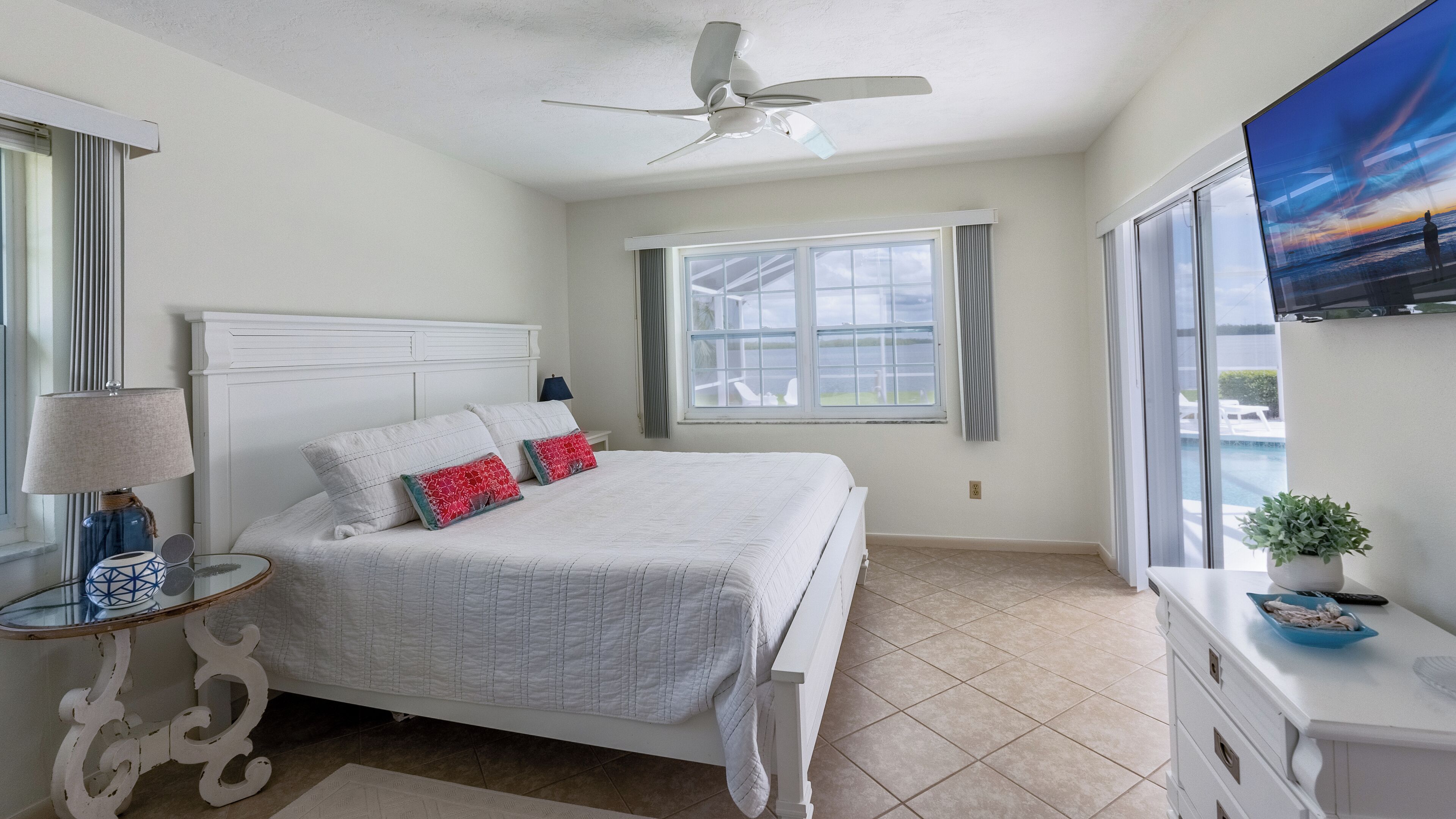 A bedroom with a bed, a ceiling fan, a window, and a TV.