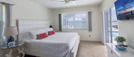 A bedroom with a bed, a ceiling fan, a window, and a TV.