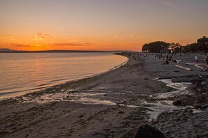 A beach with a sunset, sandy shore, and people walking.