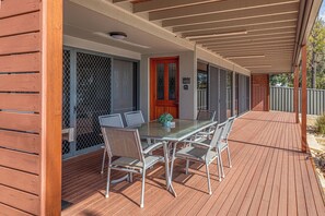 A covered outdoor patio with a glass table and metal chairs, a wooden door, and a metal fence. - Almonta Apartments on the Waterfront (B) (Coffin Bay)