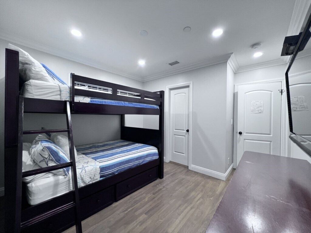 Dormitorio con literas, suelo de madera, paredes blancas y una puerta.