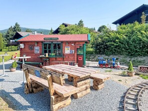 A rustic wooden building with a red roof, a small blue train, and picnic tables in front.