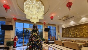 A lobby with a large Christmas tree, a chandelier, and a sofa. - APA Hotel (Vo Cuong)