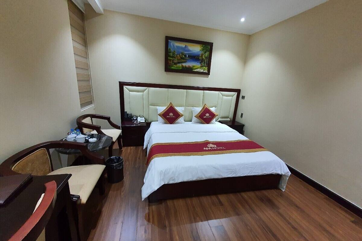 A hotel room with a large bed, two pillows, a desk with a chair, a small table, and a painting on the wall.