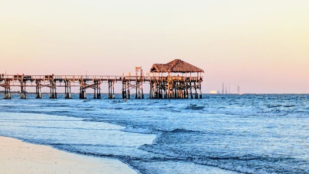 A pier extending into the sea with a thatched-roof structure at the end.