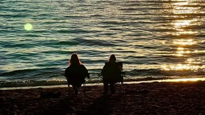 Two people sitting on chairs facing the sea at sunset with boats in the water and mountains in the background. - Spacious Cozy Home with private "HOT TUB" (Zephyr Cove)
