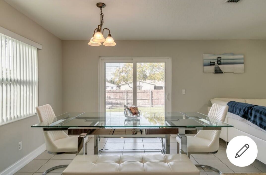 A modern dining area with a glass-top table, white chairs, and a bench. There is a hanging light fixture above the table.