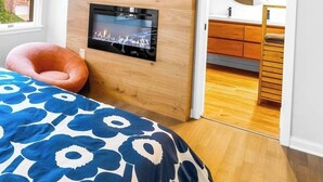 A bedroom with a wooden headboard, a TV mounted on the wall, a bed with a blue floral bedspread, and a wooden floor. - Icy mini split added, luxury, walk to Washington St, EV, Movie room, Spa bath (Bolivar)