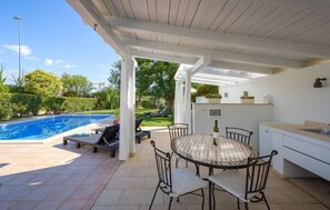 Un espacio al aire libre techado con piscina, una mesa de comedor con sillas y una zona de cocina.