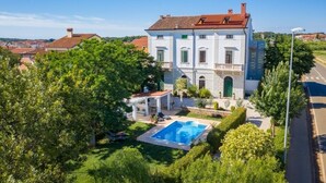 A large, two-story building with a swimming pool, surrounded by lush greenery and a clear blue sky. - Historical Villa Vigneri with pool and large garden (Novigrad)
