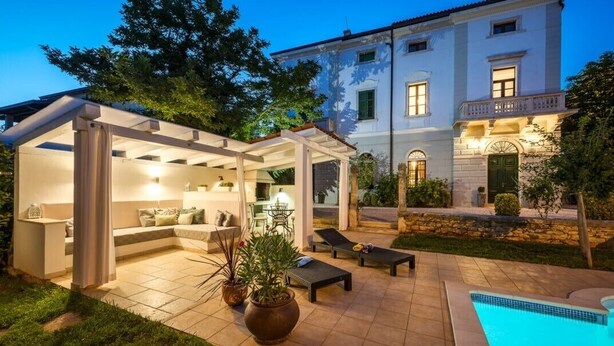 A well-lit outdoor patio with a pool, lounge chairs, and a covered seating area with a table and chairs. - Historical Villa Vigneri with pool and large garden (Novigrad)