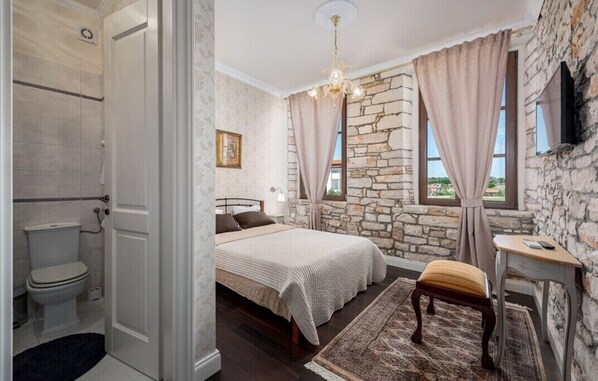 A bedroom with a stone wall, a bed with a beige blanket, a bedside table, a chair, and a window with curtains. - Historical Villa Vigneri with pool and large garden (Novigrad)
