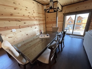 A wooden interior with a glass-top dining table, chairs, and a chandelier.