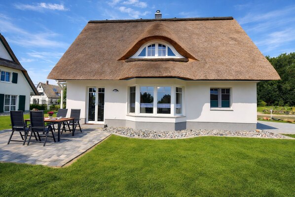 A house with a thatched roof, a patio with a table and chairs, and a well-maintained lawn.