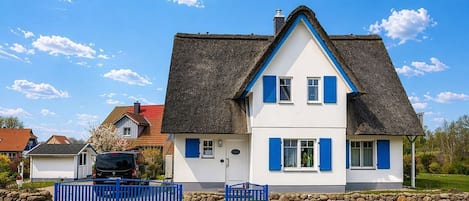 A two-story house with a steeply pitched roof, a stone foundation, and a blue fence.