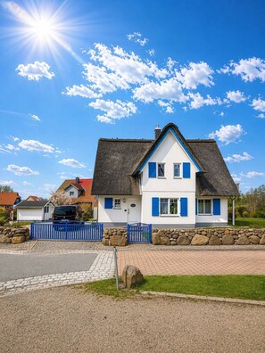 A two-story house with a steeply pitched roof, a stone foundation, and a blue fence.
