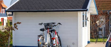 A small building with a sloped roof, two bicycles parked in front, and a car parked nearby.