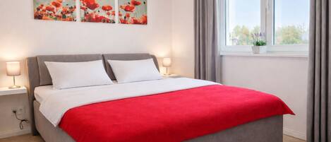 A bed with a red blanket, two bedside lamps, and three red flower paintings on the wall.