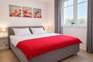 A bed with a red blanket, two bedside lamps, and three red flower paintings on the wall.