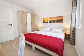 A bedroom with a bed, a wardrobe, a desk, and a window with curtains.