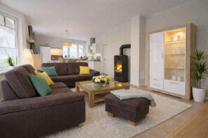 A modern living room with a sofa, ottoman, and coffee table, a fireplace, and a kitchen in the background.