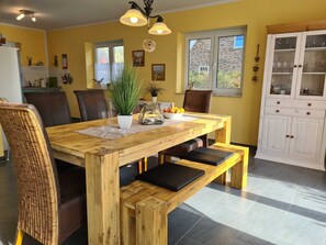 A dining area with a wooden table, chairs, and benches. There is a potted plant on the table, a bowl of fruit, and a cabinet with glass doors. - A4 Ferienhaus Sturmvogel Ostseebad Rerik / old = sold - A4: 4-room (Rerik (Ostseebad))