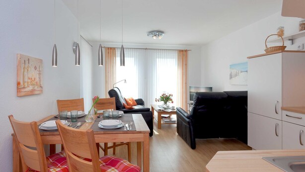 En moderne stue med spiseplads, sofa, fjernsyn og køkken.