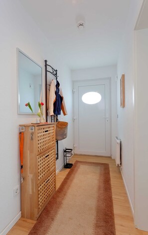 A hallway with a wooden cabinet, a mirror, a coat rack, and a door with a light fixture. - 1.1 - Glienbergweg 26 Zinnowitz (Zinnowitz)