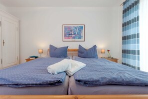 Un lit double avec une literie bleue, deux oreillers, une serviette blanche, un tableau abstrait encadré accroché au mur et une fenêtre avec des rideaux bleus.