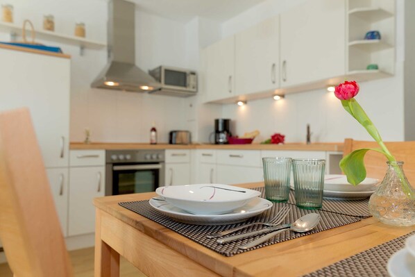 A dining table set with plates, glasses, and cutlery, a vase with a flower, and a microwave above the cabinets.