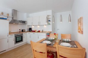 Une cuisine moderne avec des meubles blancs, un four à micro-ondes, un four traditionnel et un coin repas avec une table mise pour deux personnes.