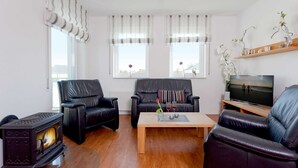 Ein Wohnzimmer mit Kamin, zwei Ledersofas, einem Couchtisch und einem Fernseher.