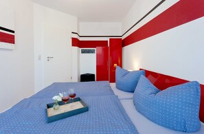 A modern hotel room with a bed, a tray with wine glasses, and a red and white color scheme.