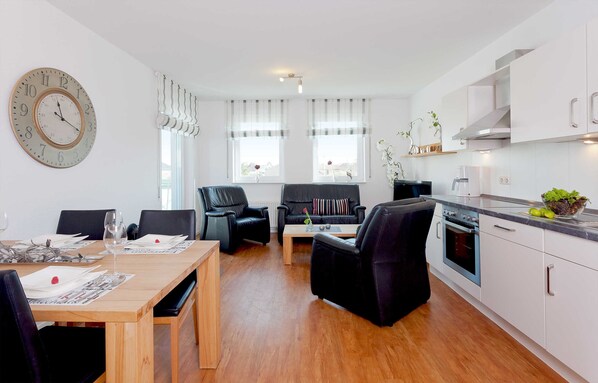 Un salón moderno con una mesa de comedor, sofás de cuero negro y una zona de cocina con armarios blancos y horno empotrado.