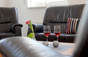 A living room with a black leather sofa, two wine glasses on a table, and a vase with a single red flower.