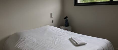 Een hotelkamer met een bed, een nachtkastje, een raam met uitzicht op groen en bergen, en een vaas op het nachtkastje.