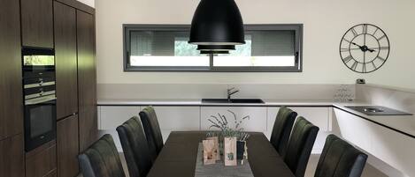 Una cocina moderna con comedor, que incluye una mesa grande, sillas, una lámpara colgante, una ventana y un reloj de pared.