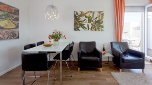 A modern dining area with a white table, black chairs, a vase of flowers, and a painting of leaves. - 2.3 - Glienbergweg 26 a Zinnowitz (Zinnowitz)